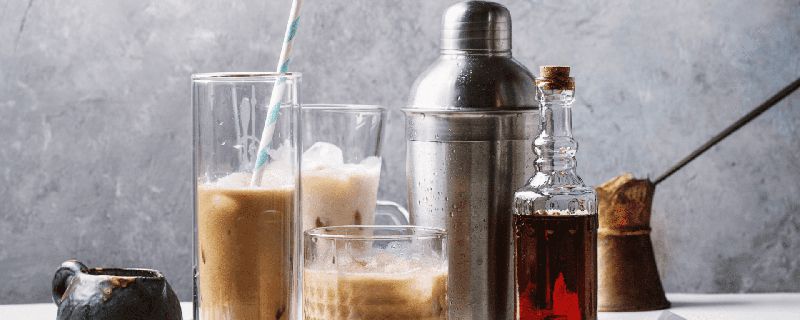Verschiedene Gläser und Flaschen mit Kaffeegetränken und einem Shaker auf einem Tisch.